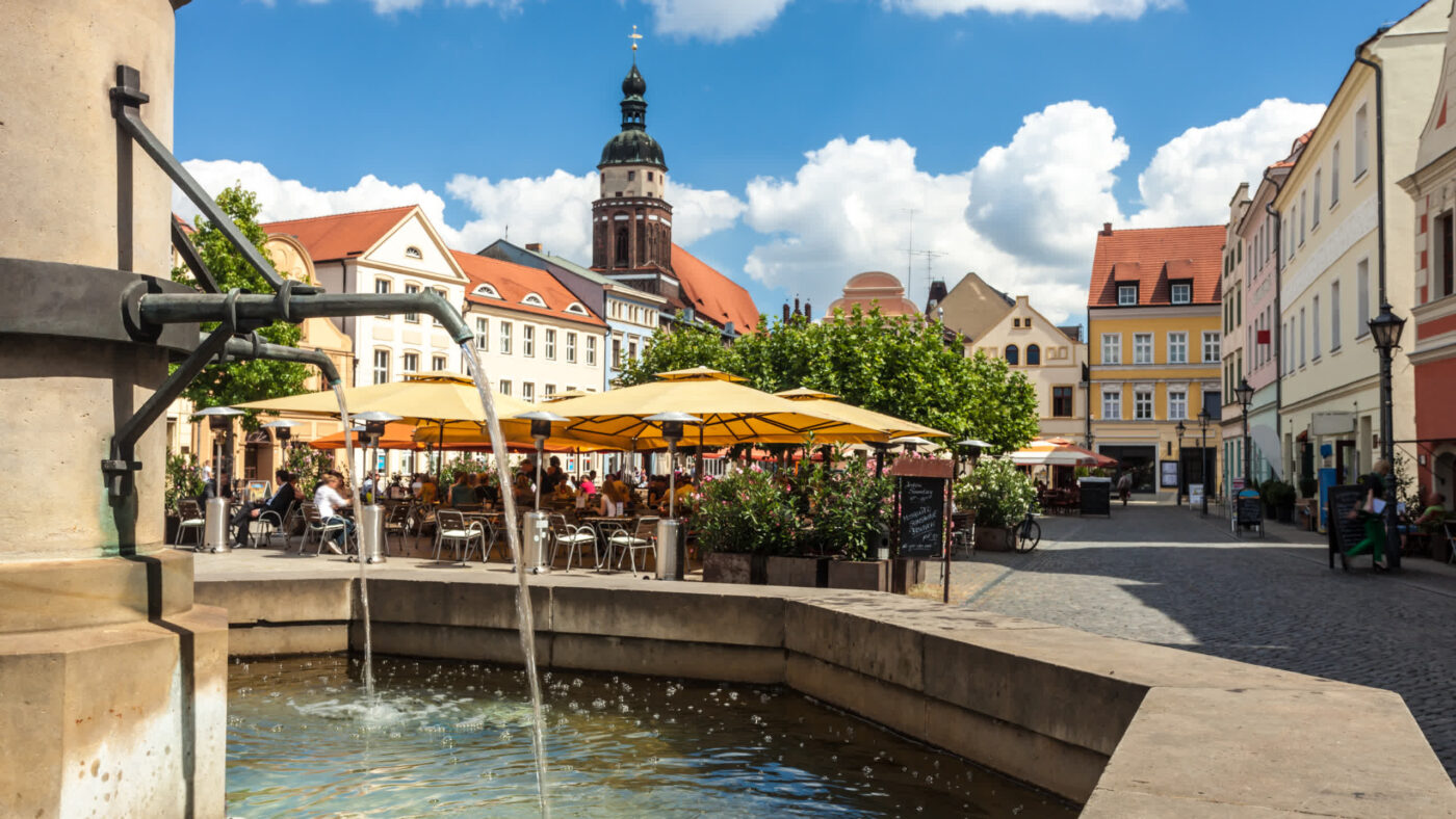 Lokal: Der Cottbuser Altmarkt in der Lausitz, im Vordergrund der Brunnen, im Hintergrund der Altmarkt bei Sommer und die Oberkirche.
