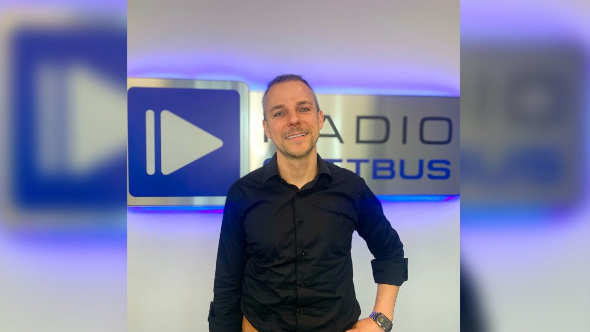 Rico Nattke vom Ingeneurbüro Lausitz IB Lausitz vor dem Radio Cottbus Logo im Mai 2023