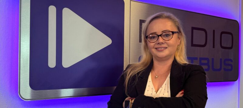 Roksana Müller Mediaberaterin von Radio Cottbus steht vor dem Logo des Medienunternehmens