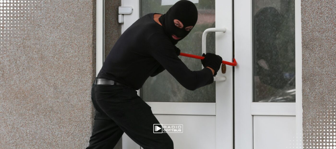 Eine vermummte Person in schwarzer Kleidung versucht in eine Wohnung einzubrechen und hebelt die Tür auf.