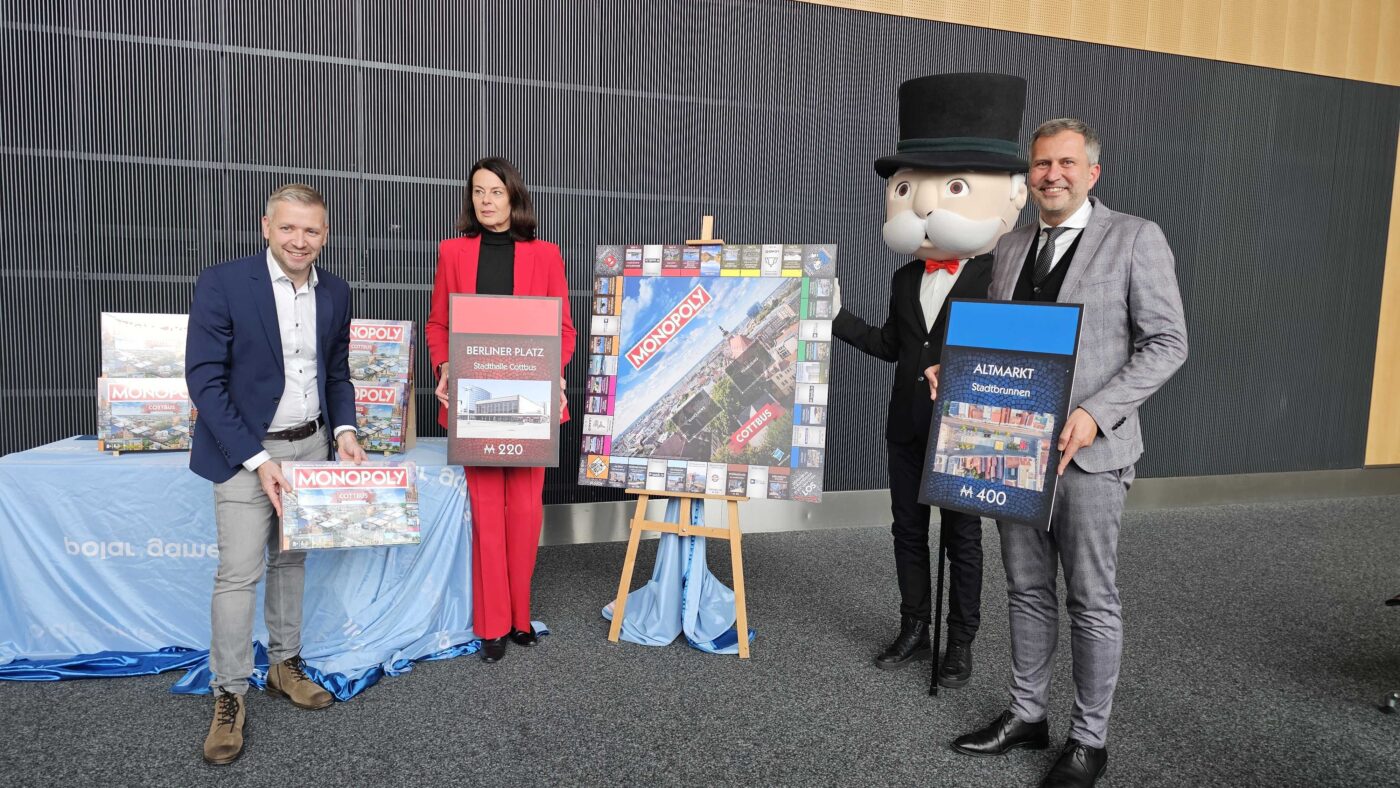 Florian Freitag (Geschäftsführer von Polar Games), Daniela Kerzel (Geschäftsführerin CTM Cottbus) und Oberbürgermeister Tobias Schick stehen vor einem Tisch mit dem neuen Cottbuser Monopoly.
