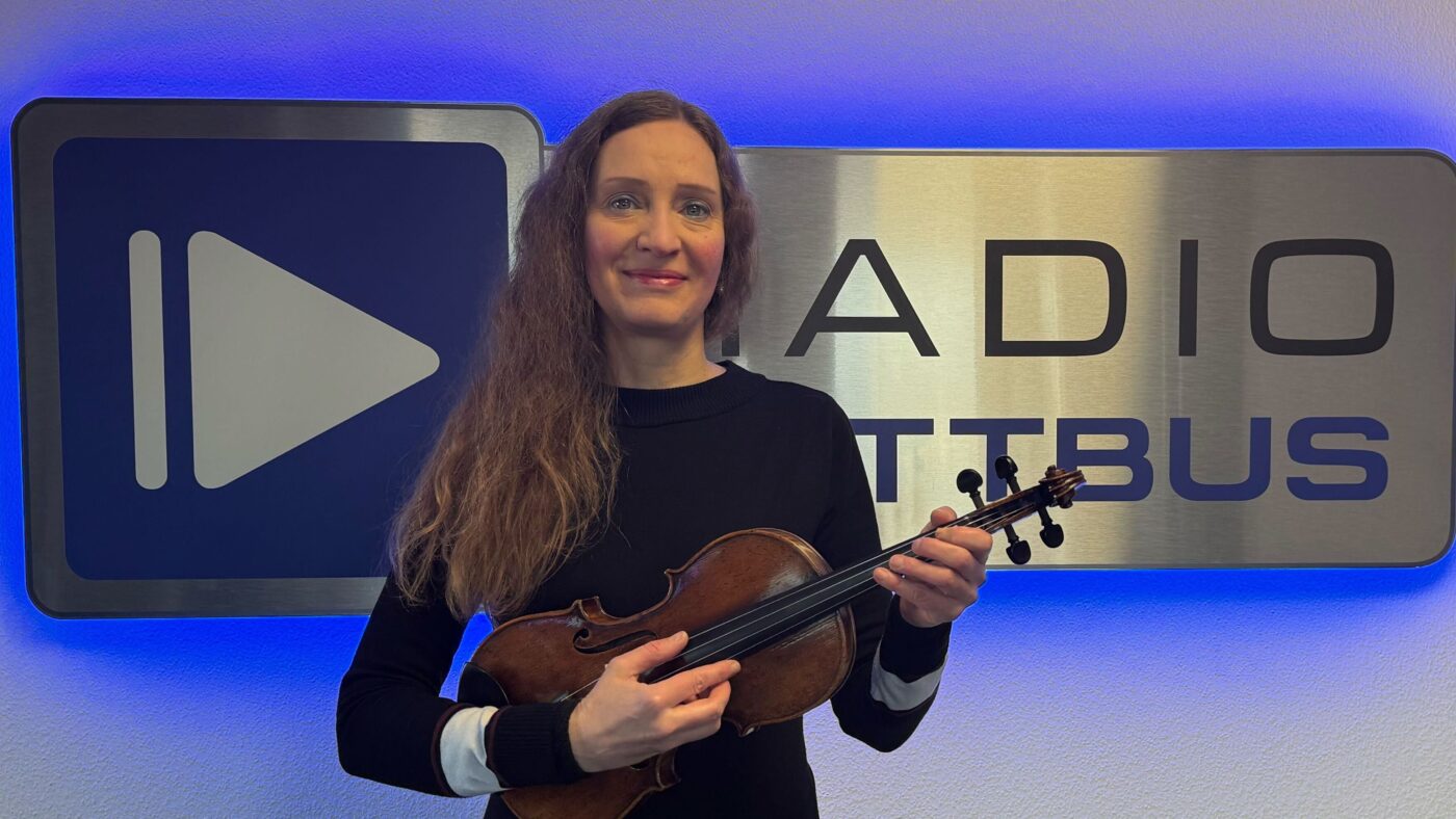 Anke Wingrich mit ihrer Geige vor dem Radio Cottbus Logo