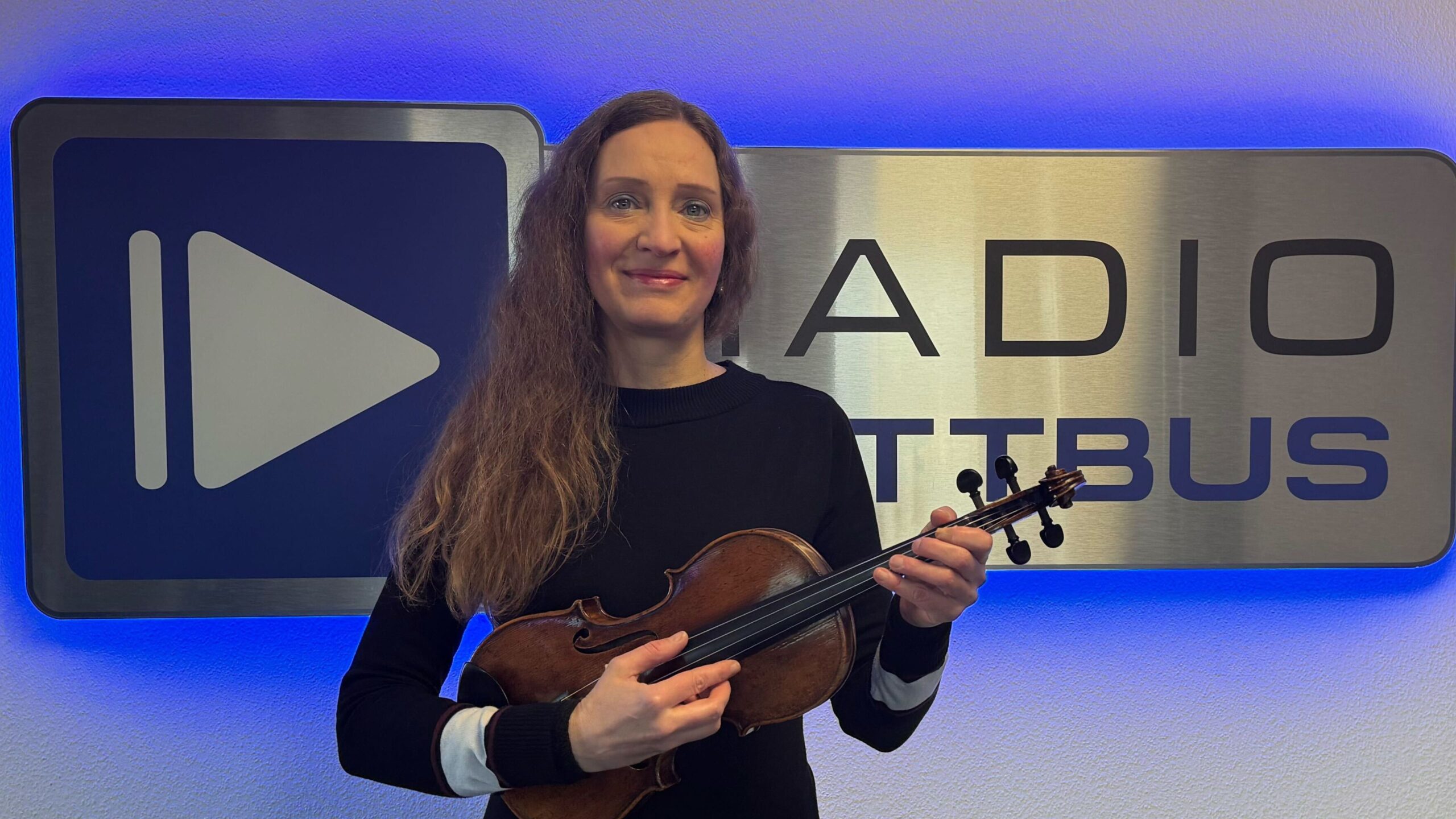 Anke Wingrich mit ihrer Geige vor dem Radio Cottbus Logo