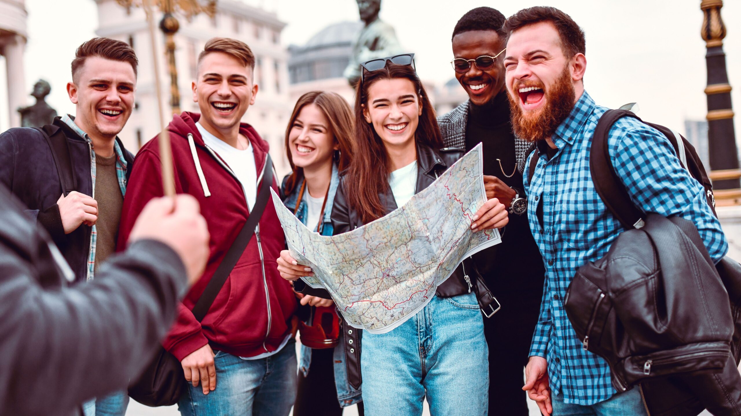 Eine Gruppe aus Freunden macht eine Stadttour, lacht und die Frau in der Mitte hat einen Stadtplan in der Hand