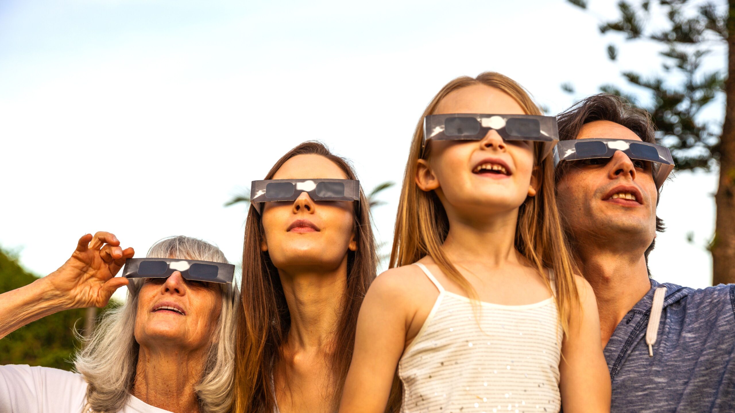 eine Familie aus Oma, Mama, Tochter und Papa tragen Schutzbrillen und schauen sich die Sonnenfinsternis an