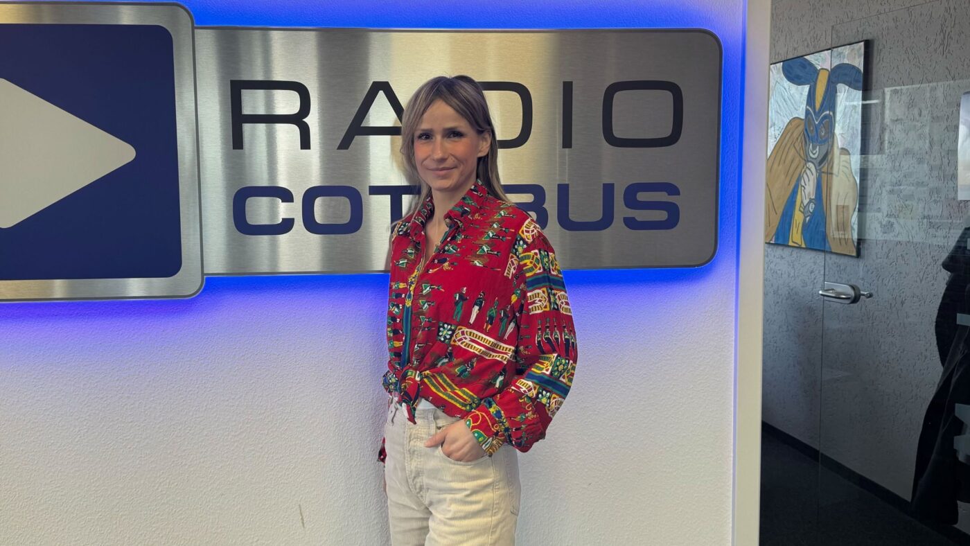 Chefin on Air Carolin Puscha vor dem Radio Cottbus Logo