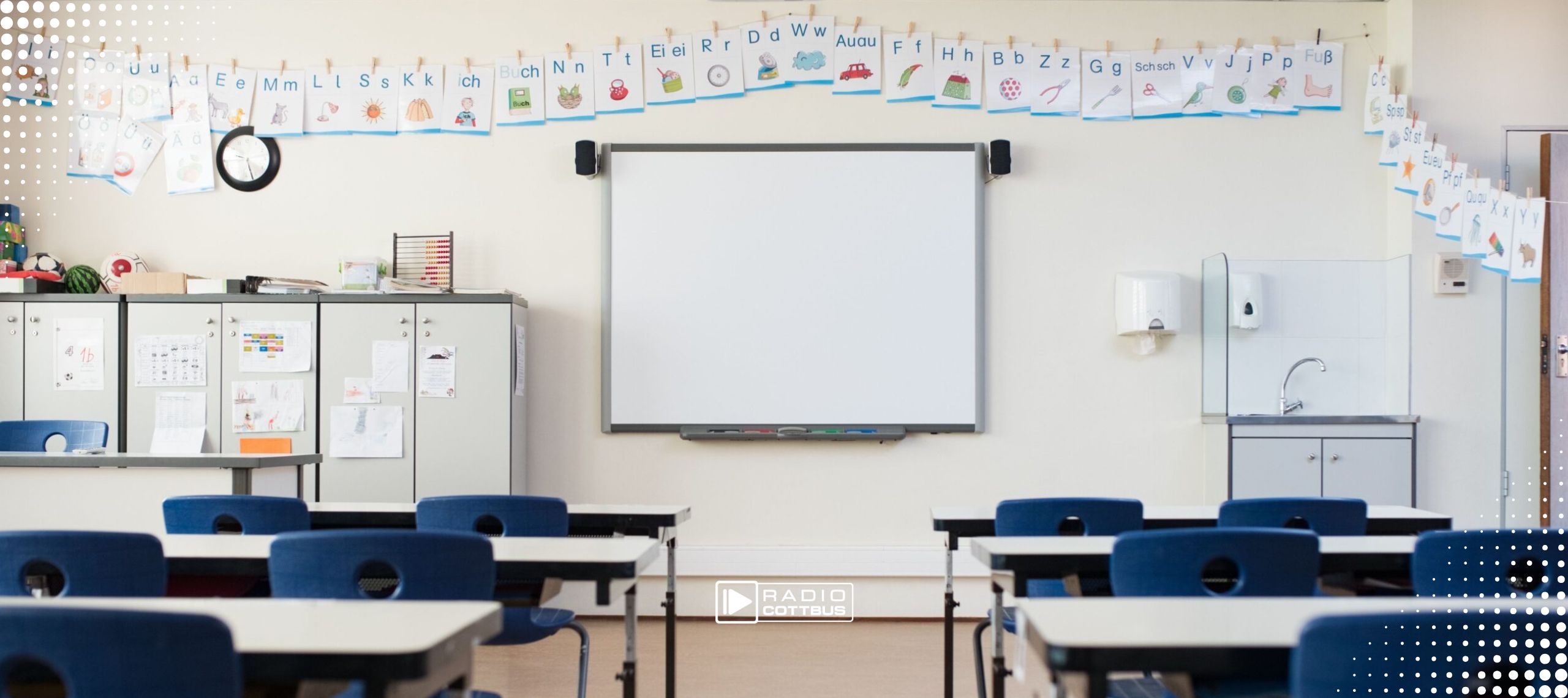 Ein leeres Klassenzimmer. Darin stehen Schulbänke mit Stühlen, vorne ist eine weiße Tafel