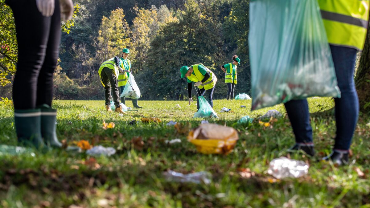 Mehrere Menschen mit grünen Warnwesten räumen einen Park auf mit Müllbeuteln und Müll-Zangen