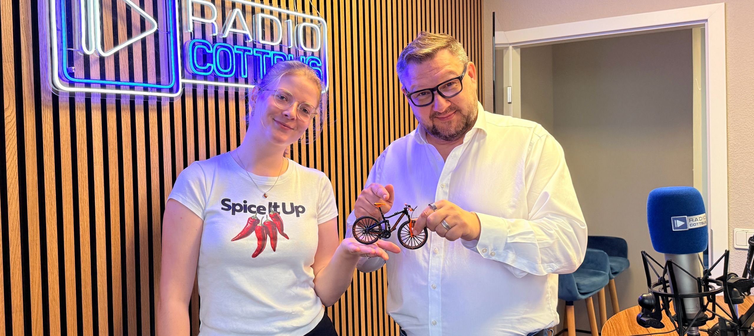 Luka Stadelmeier und Ronny Gersch stehen im Studio und halten das Modell eines Fahrrads in der Hand