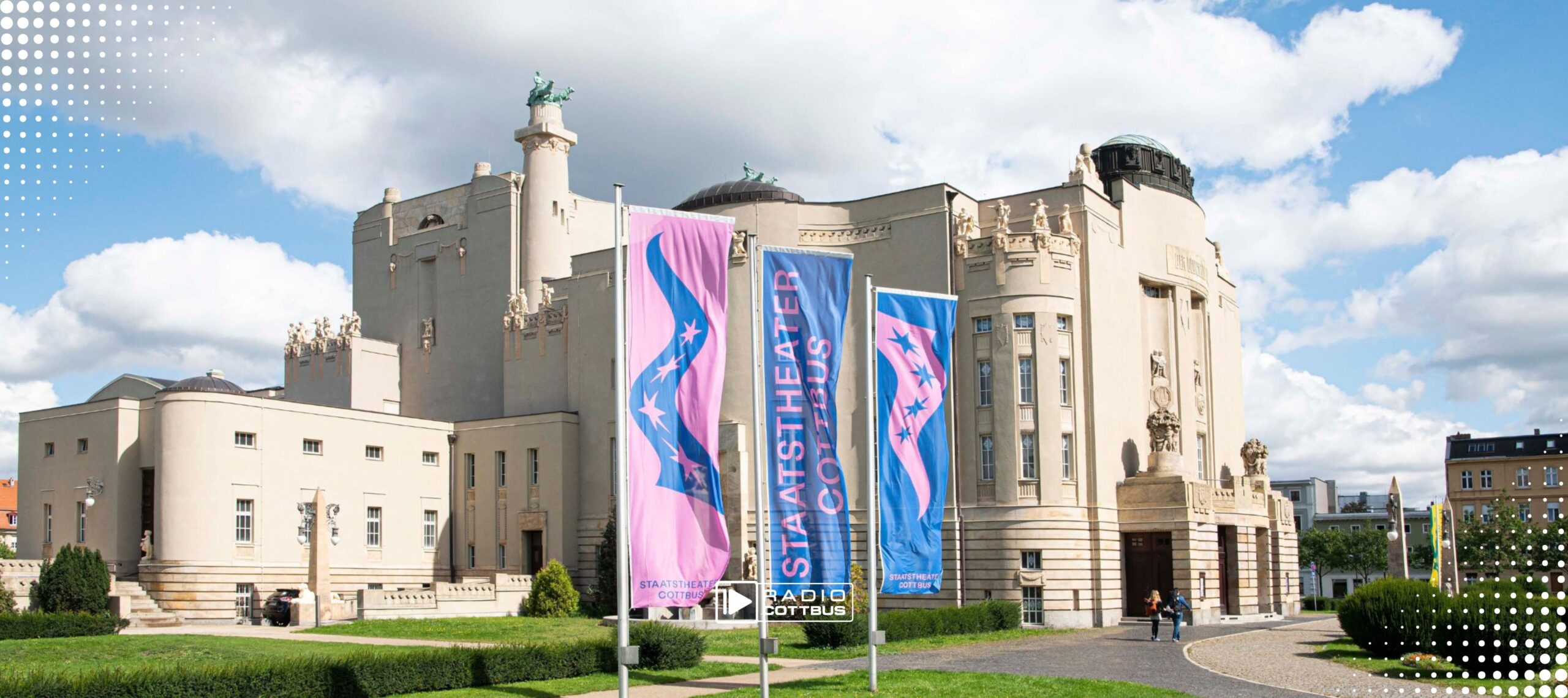 Eine Komplettansicht des Staatstheater Cottbus im Sommer mit drei großen Fahnen vor dem Großen Haus am Schillerplatz