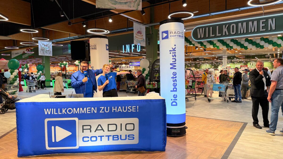 Die Wacher Macher Ronny und Luka stehen hinzer einem Radio Cottbus Tresen im Lausitz Park vor dem Marktkauf. Drum herum sind viele Menschen.