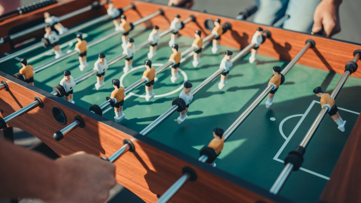 Zwei Männer spielen Tischkicker gegeneinander, man sieht nur ihre Hände und den Tischkicker mit den Figuren