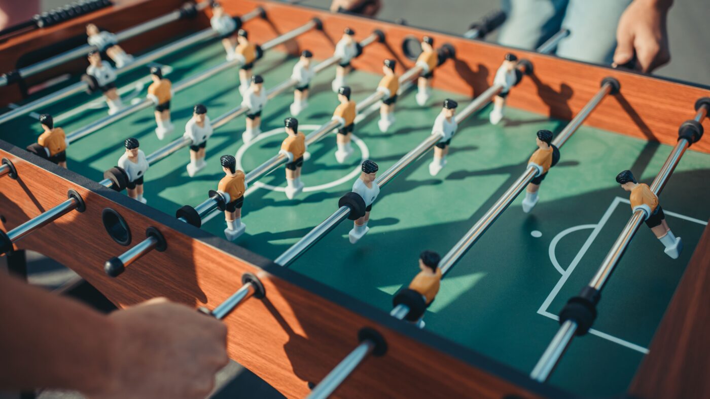 Zwei Männer spielen Tischkicker gegeneinander, man sieht nur ihre Hände und den Tischkicker mit den Figuren