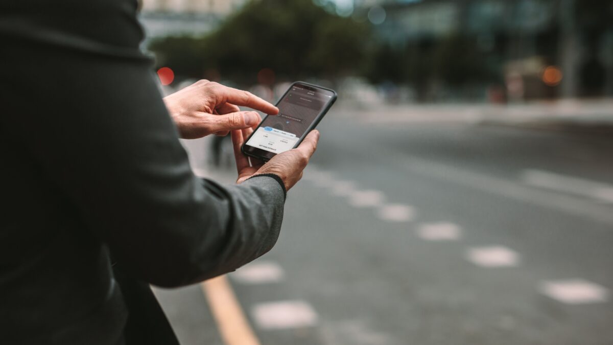 Ein Mann an einer Straße, der sein Handy in der Hand hält und darauf etwas anklickt