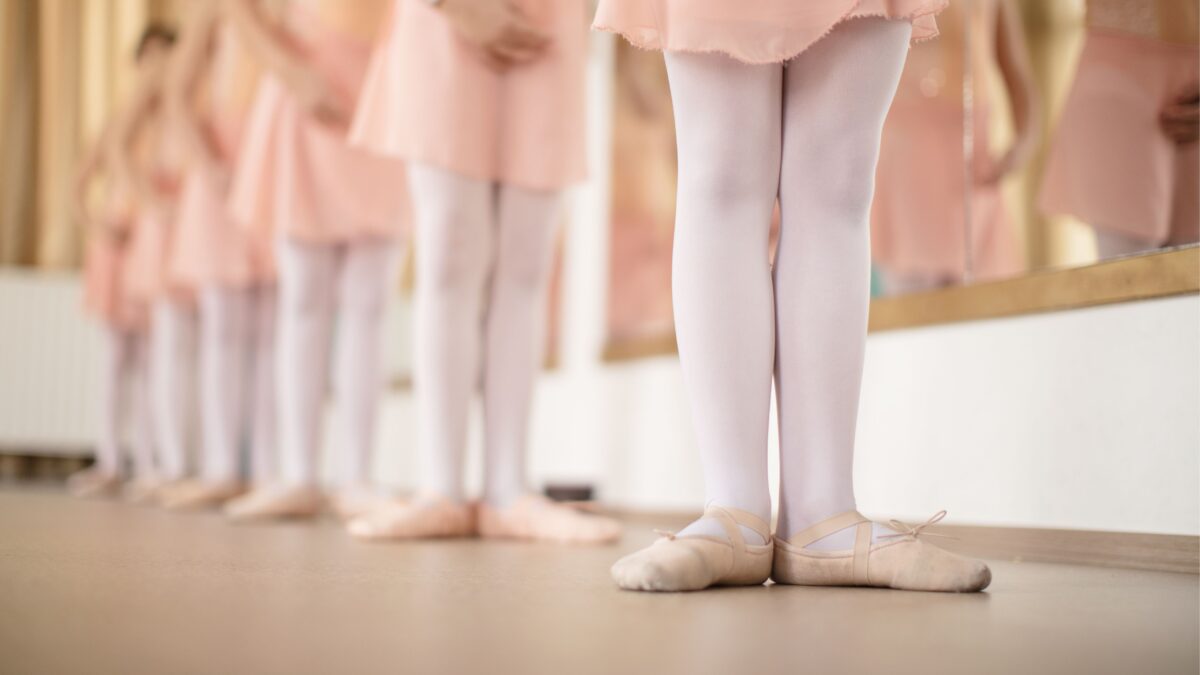 Mehrere kleine Mädchen stehen hintereinander an der Ballettstange und tragen Ballettschuhe