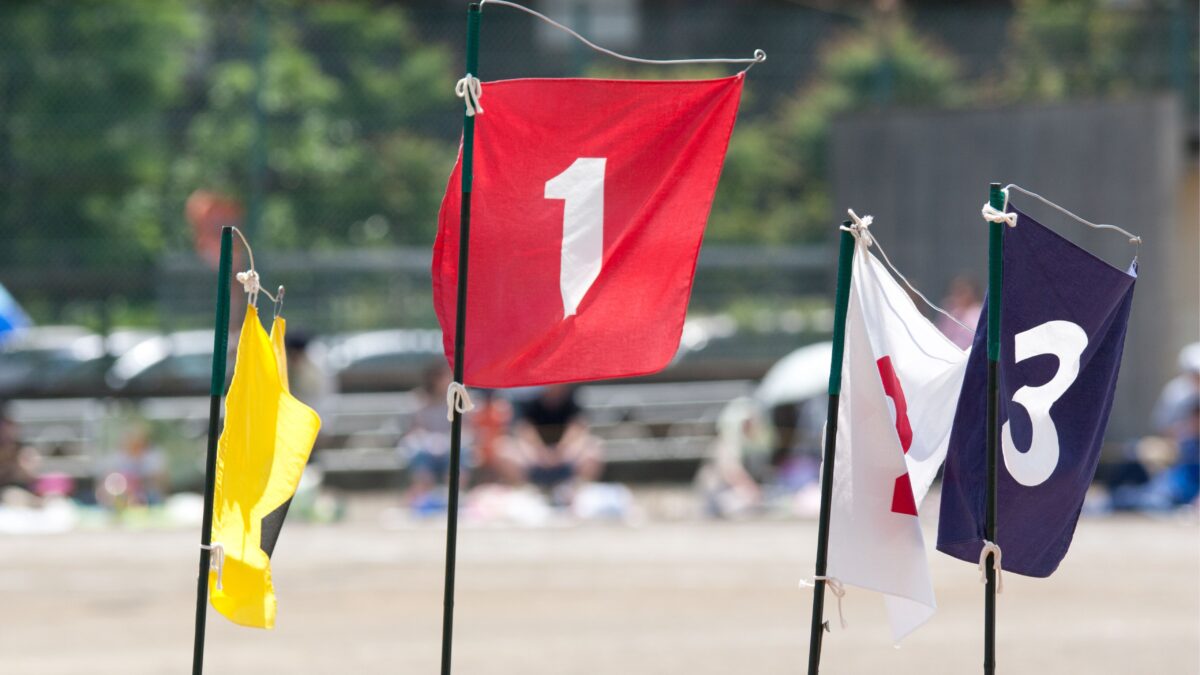 Vier Fahnen in gelb, rot, weiß und blau mit den Zahlen eins bis vier drauf. Die Fahnen stehen an einem Strand