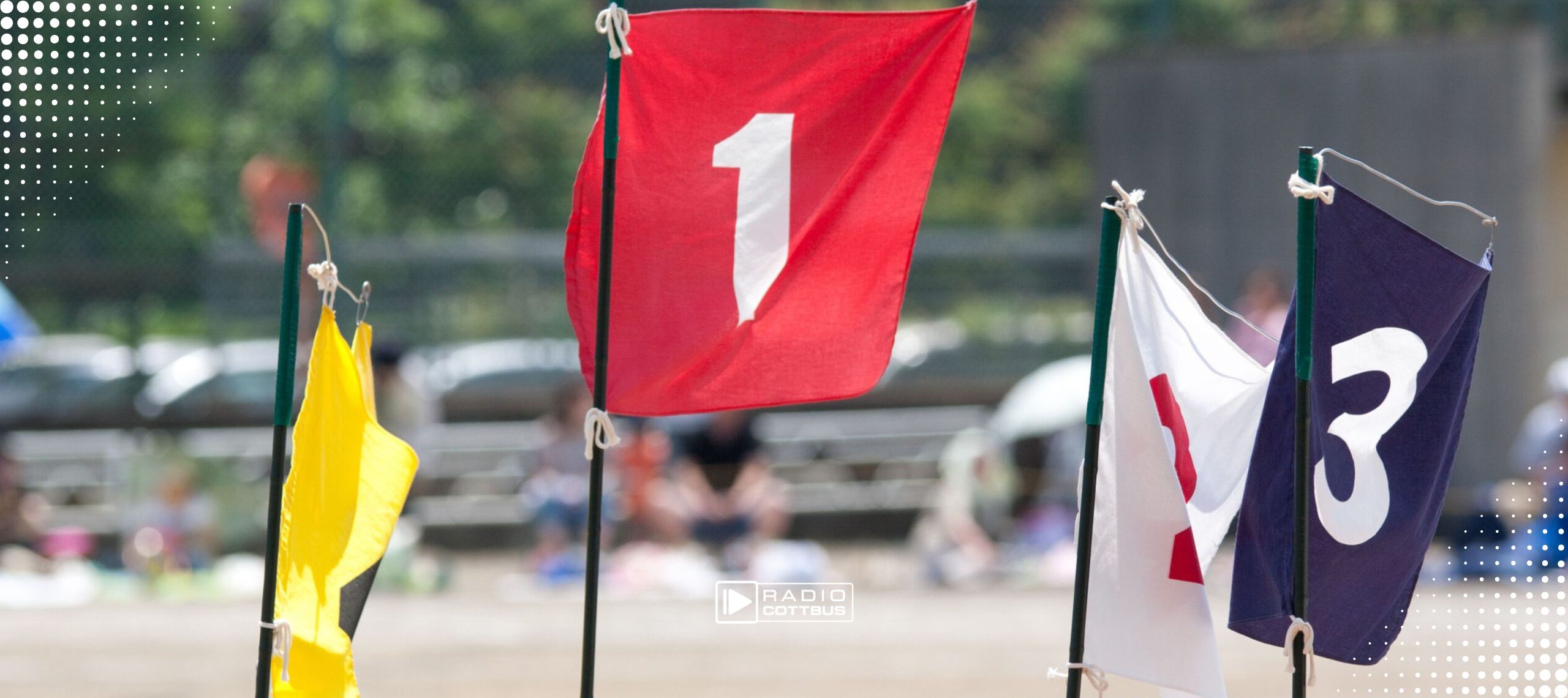 Vier Fahnen in gelb, rot, weiß und blau mit den Zahlen eins bis vier drauf. Die Fahnen stehen an einem Strand