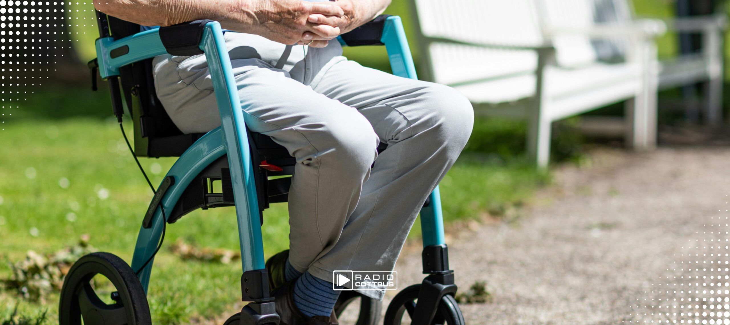 Ein älterer Mann sitzt auf einem Rollator neben einer weißen Parkbank