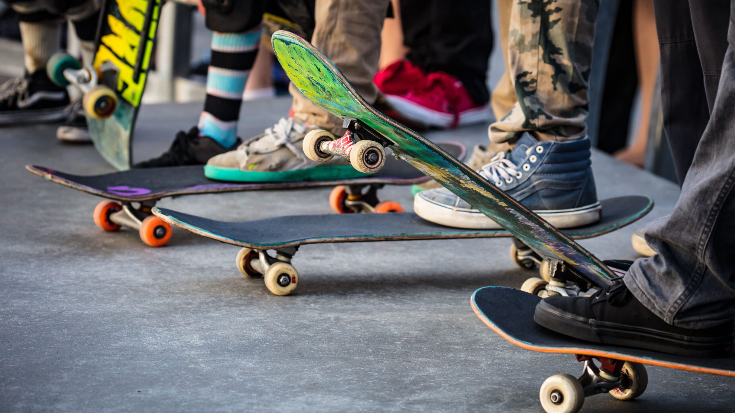 Viele Skateboards nebeneinander und Kinder, die jeweils mit einem Bein auf den einzelnen Skateboard stehen
