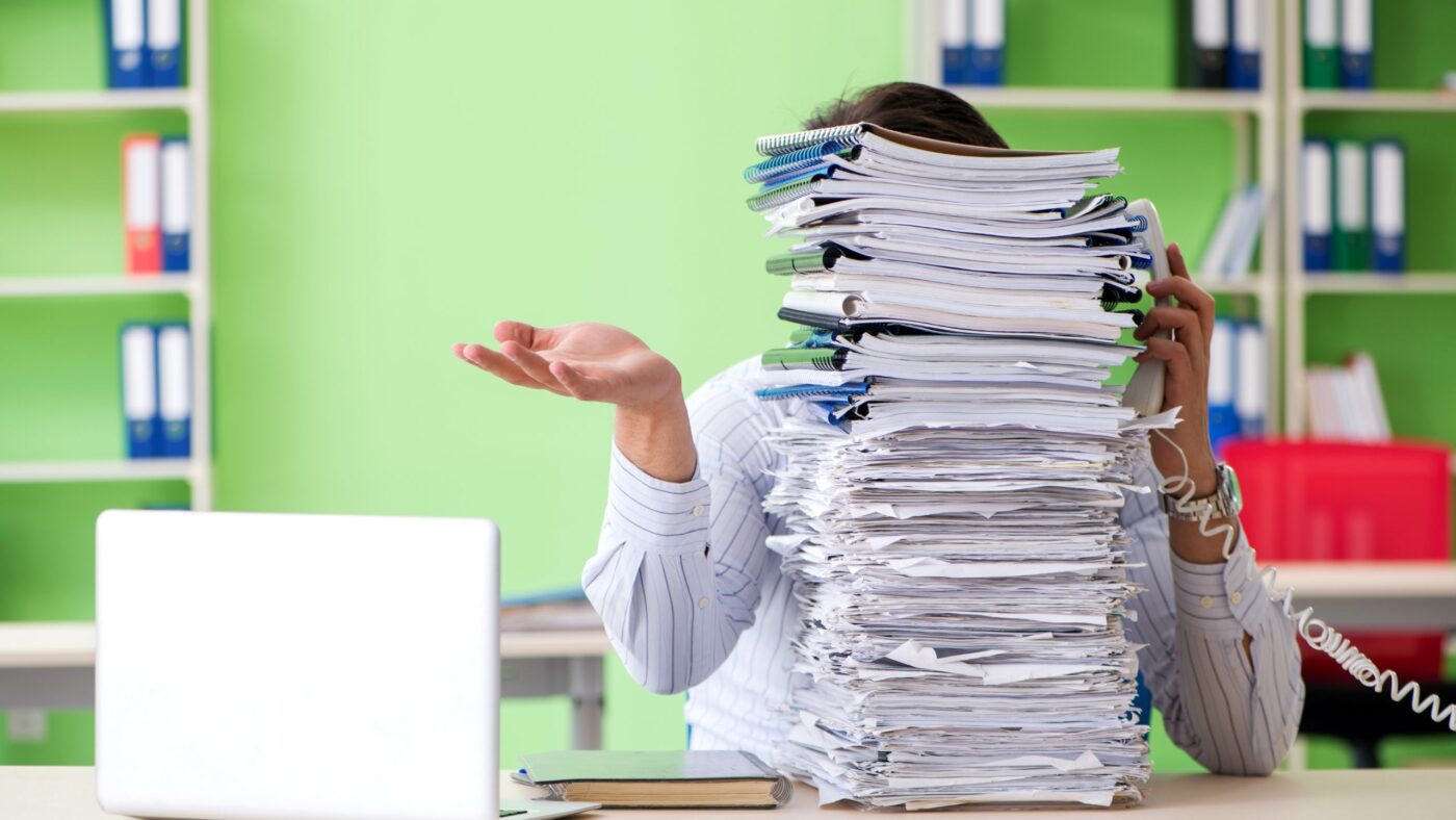 Eine Frau welche von einem Stapel Papier verdenkt wird