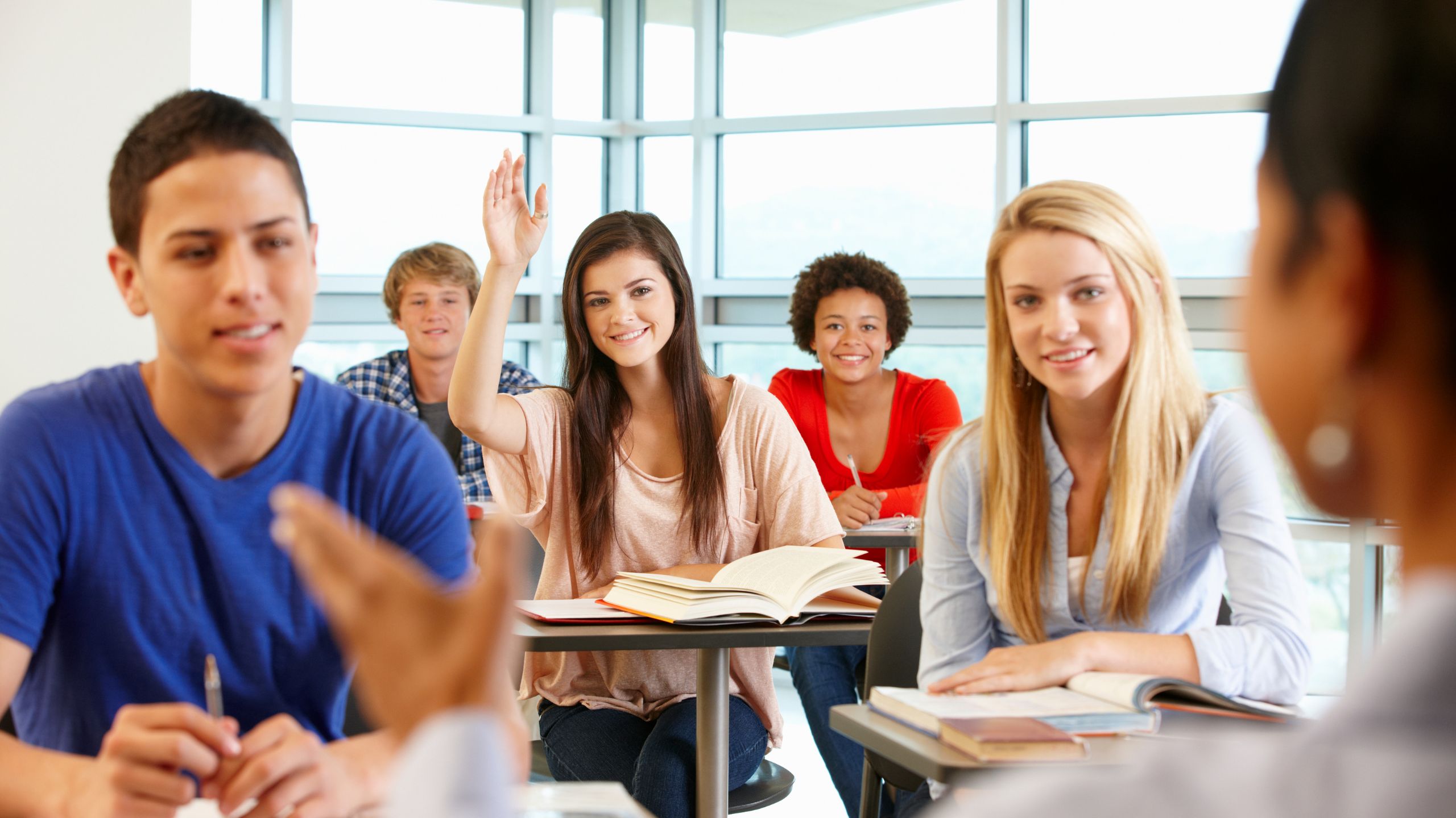 5 Schüler in einem Klassenraum - eine meldet sich und lächelt