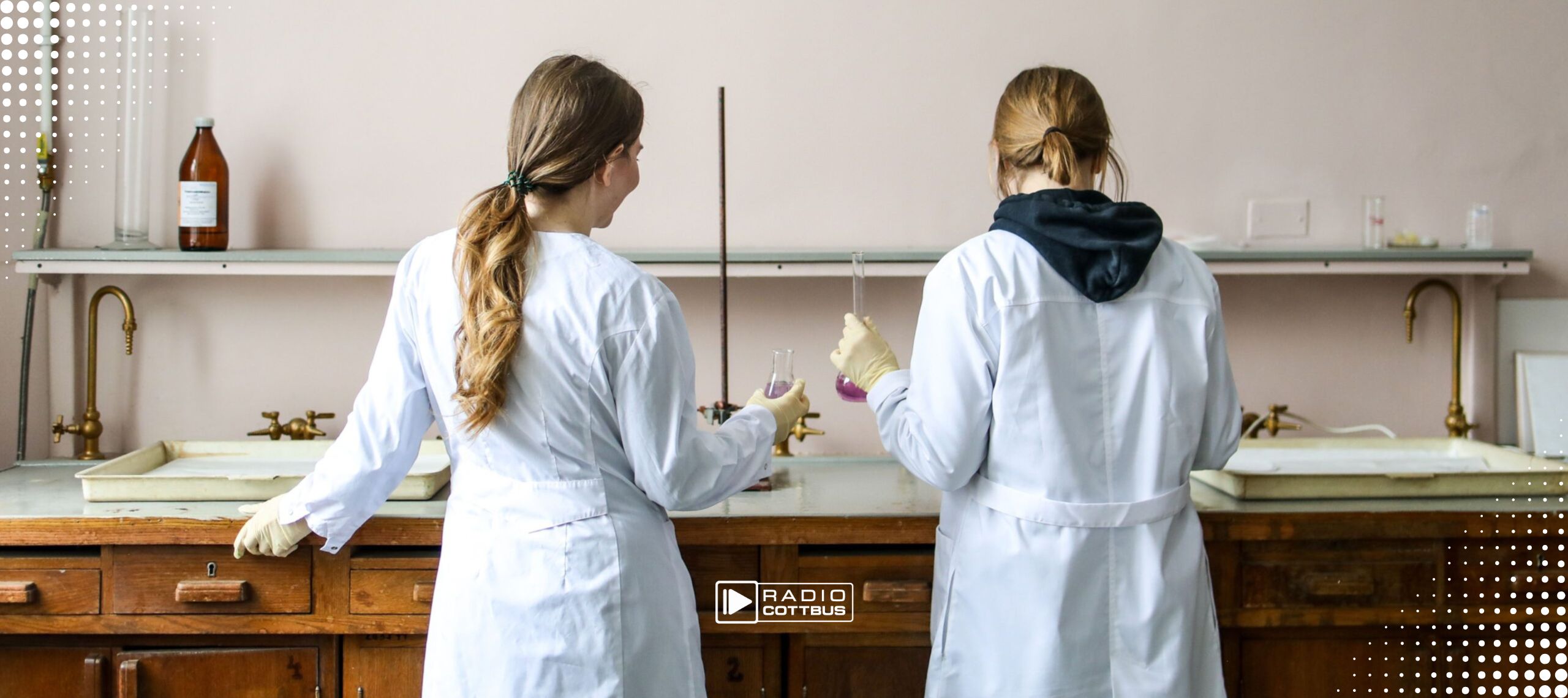 Zwei Frauen in Laborkitteln stehen an einem Tisch und experimentieren mit Gläsern