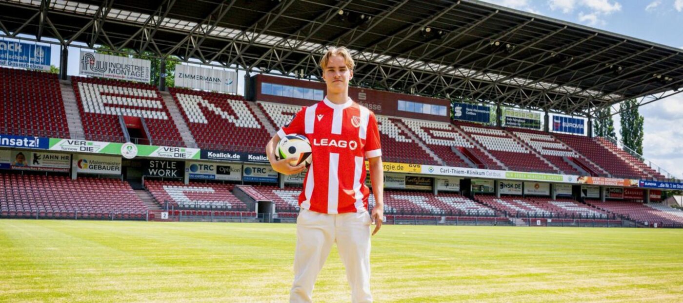 Lukas Michelbrink vom FC Energie Cottbus steht direkt nach seiner Verpflichtung auf dem Rasen im LEAG Energie Stadion, hat das Energie-Trikot übergezogen und hält einen Ball in der rechten Hand