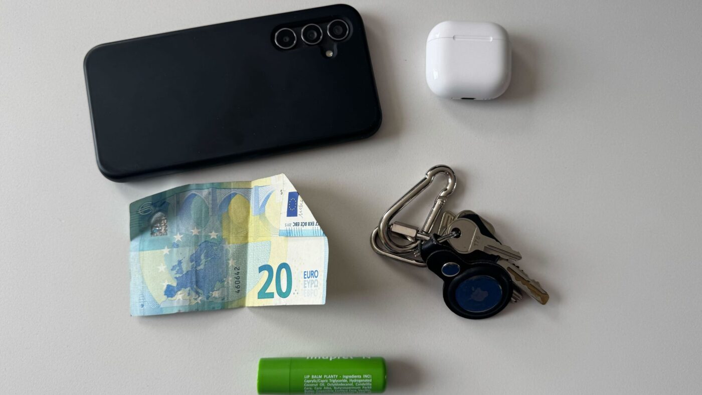 Ein Handy, ein Paar Kopfhörer, ein 20 Euro Schein, Schlüssel und ein Lippenstift liegen auf dem Tisch
