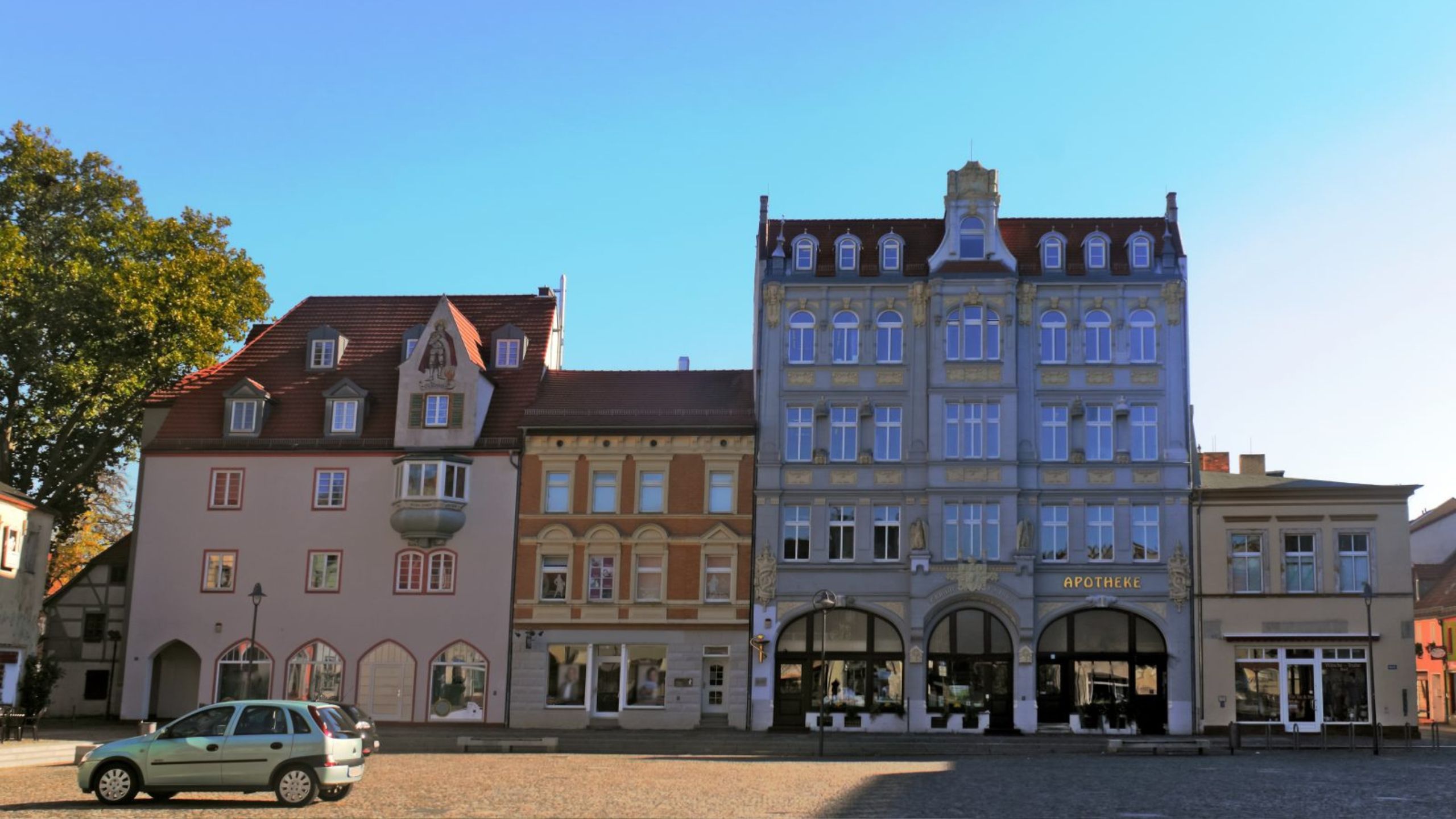 Blick auf Senftenberger Fassaden mit dem grauen Haus der Apotheke rechts und zwei weitere kleinere Häuser links davon.