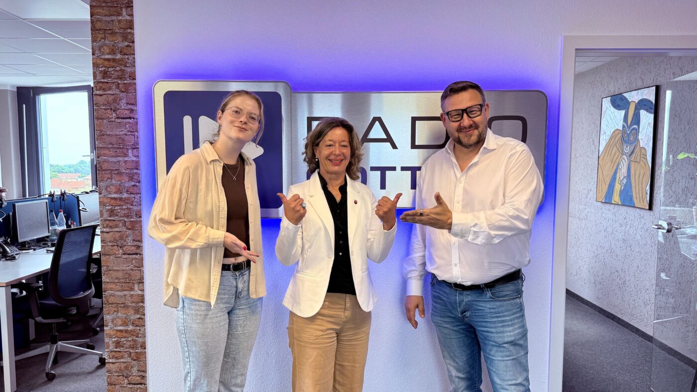 Luka Stadelmeier, Eike Belle und Ronny Gersch (von links nach rechts) stehen vor dem Radio Cottbus Logo.