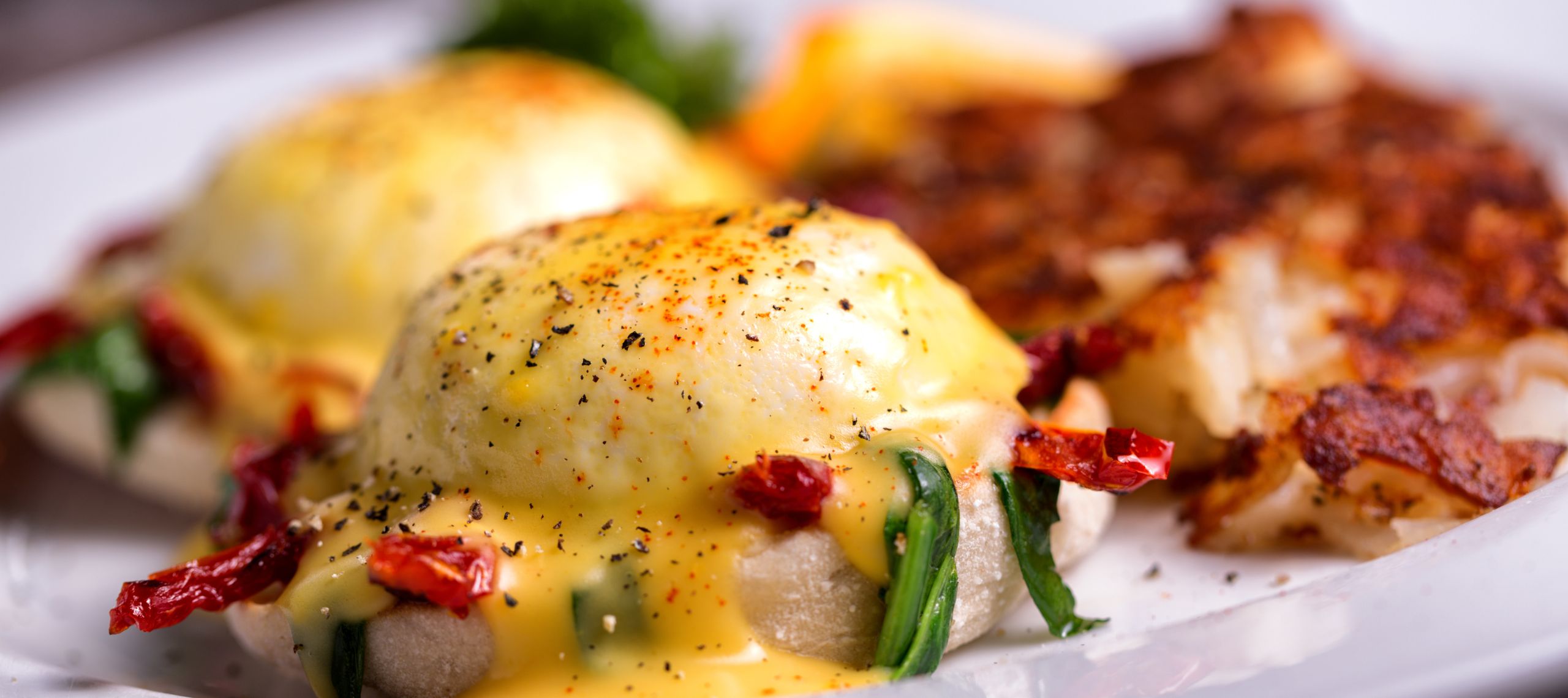 Der Frühstücksklassiker Eier Benedict zweimal angerichtet mit zwei Eiern unter Sauce Hollandaise auf einem Teller.