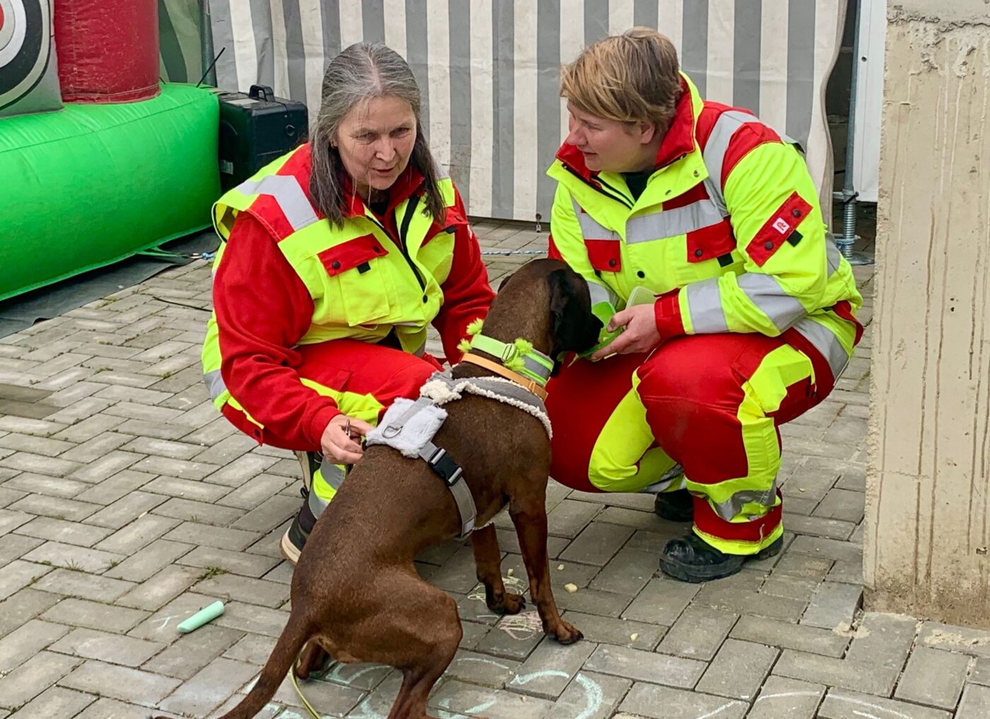2 Personen von der Regieeinheit Rettungshundestaffel Landkreis Spree Neiße mit ihrem Hund vor einem Gebäude.