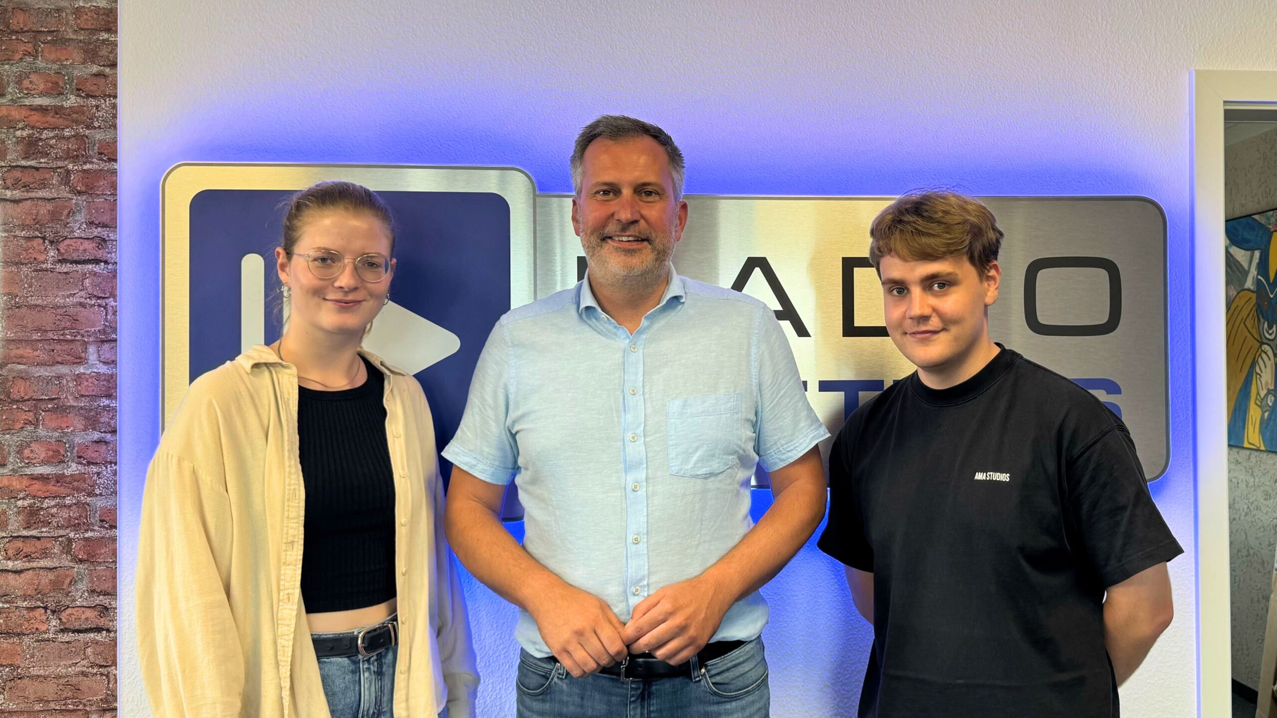 Luka Stadelmeier, Oberbürgermeister Tobias Schick und Björn Dymke (von links nach rechts) posieren vor dem Logo von Radio Cottbus
