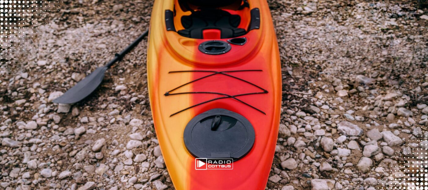 Ein rot-orangenes Kajak liegt auf einem Kieselstrand