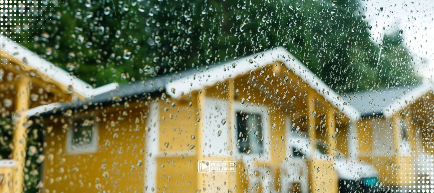 Mehrere gelbe Campingbungalows aus Holz, davor eine Scheibe mit Regen