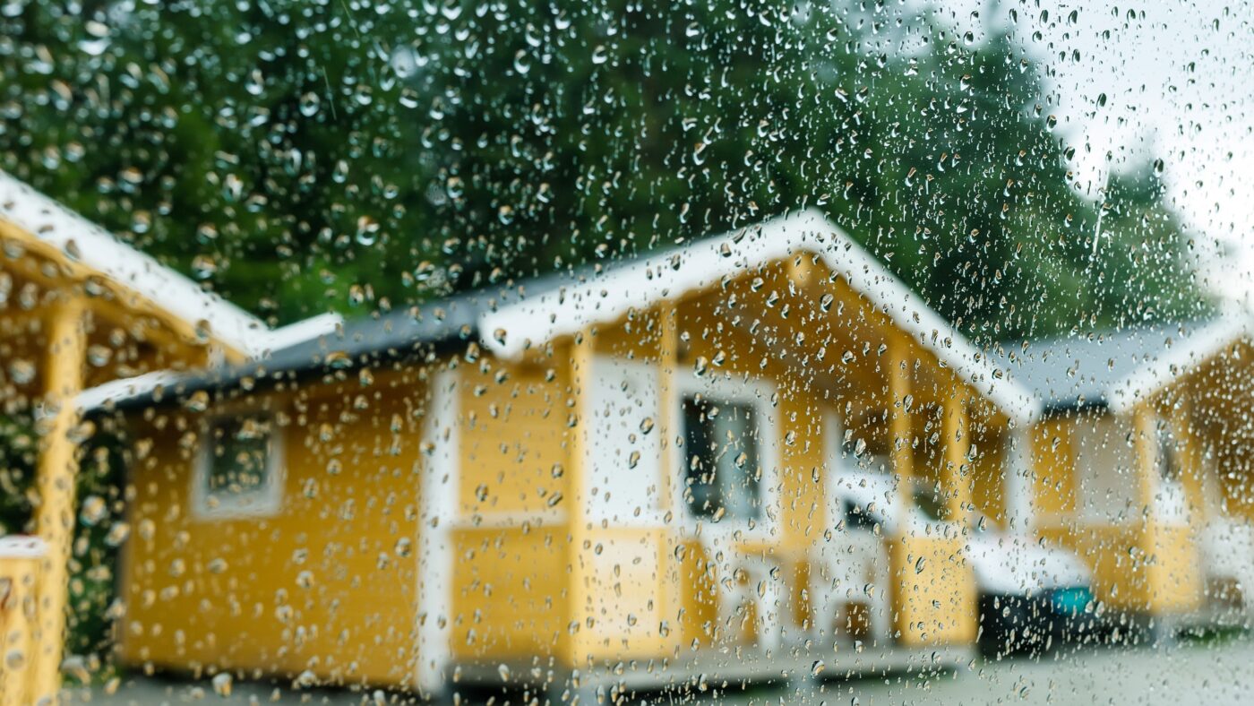 Mehrere gelbe Campingbungalows aus Holz, davor eine Scheibe mit Regen