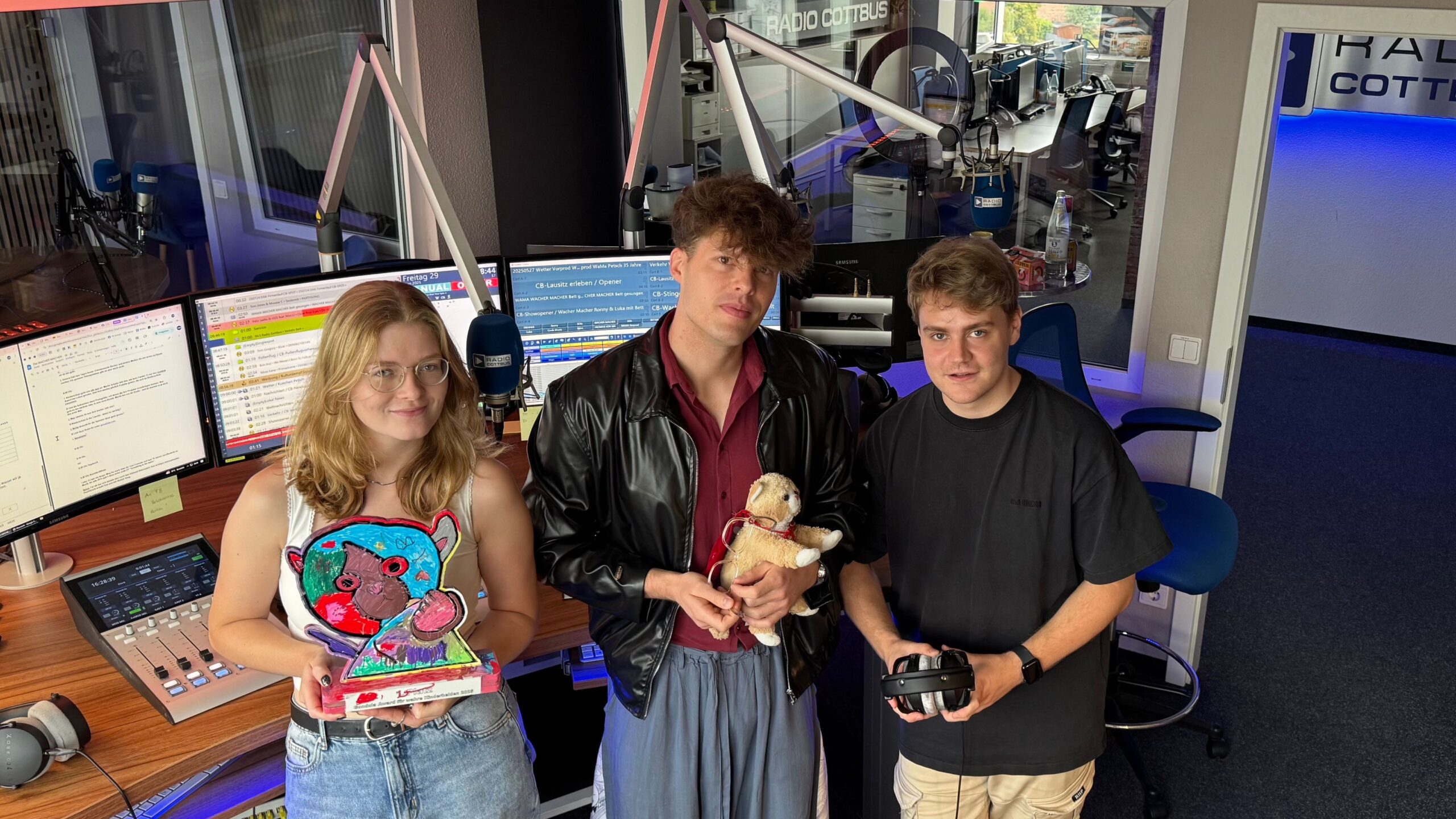 Aufnahme von Luka Stadelmeier, Martin Schüler und Björn Dymke (von links nach rechts) im Radio Cottbus Studio vor den Bildschirmen. Luka hält den Gondula Award in der Hand, Martin Schüler die Katze Gondula