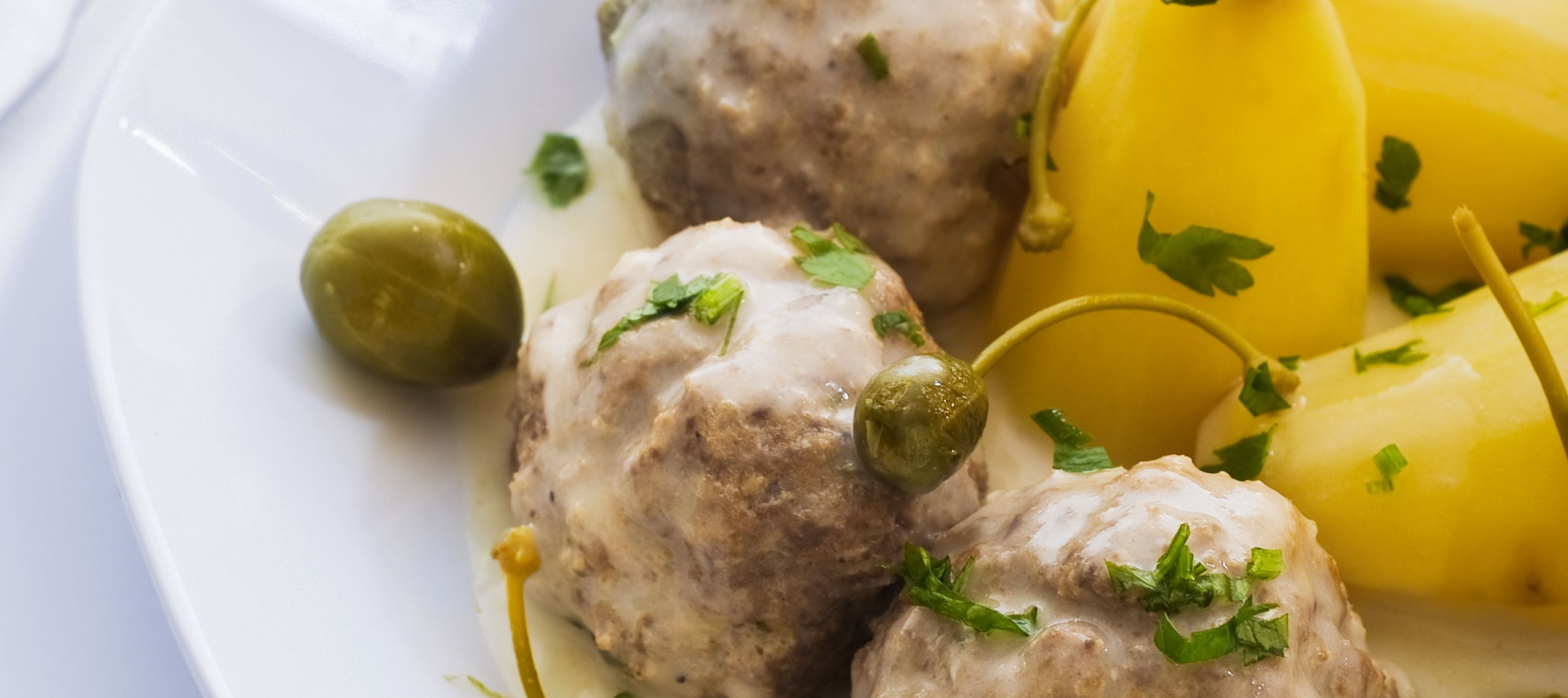Königsberger Klopse angerichtet mit Salzkartoffeln und Kapern auf einem Teller