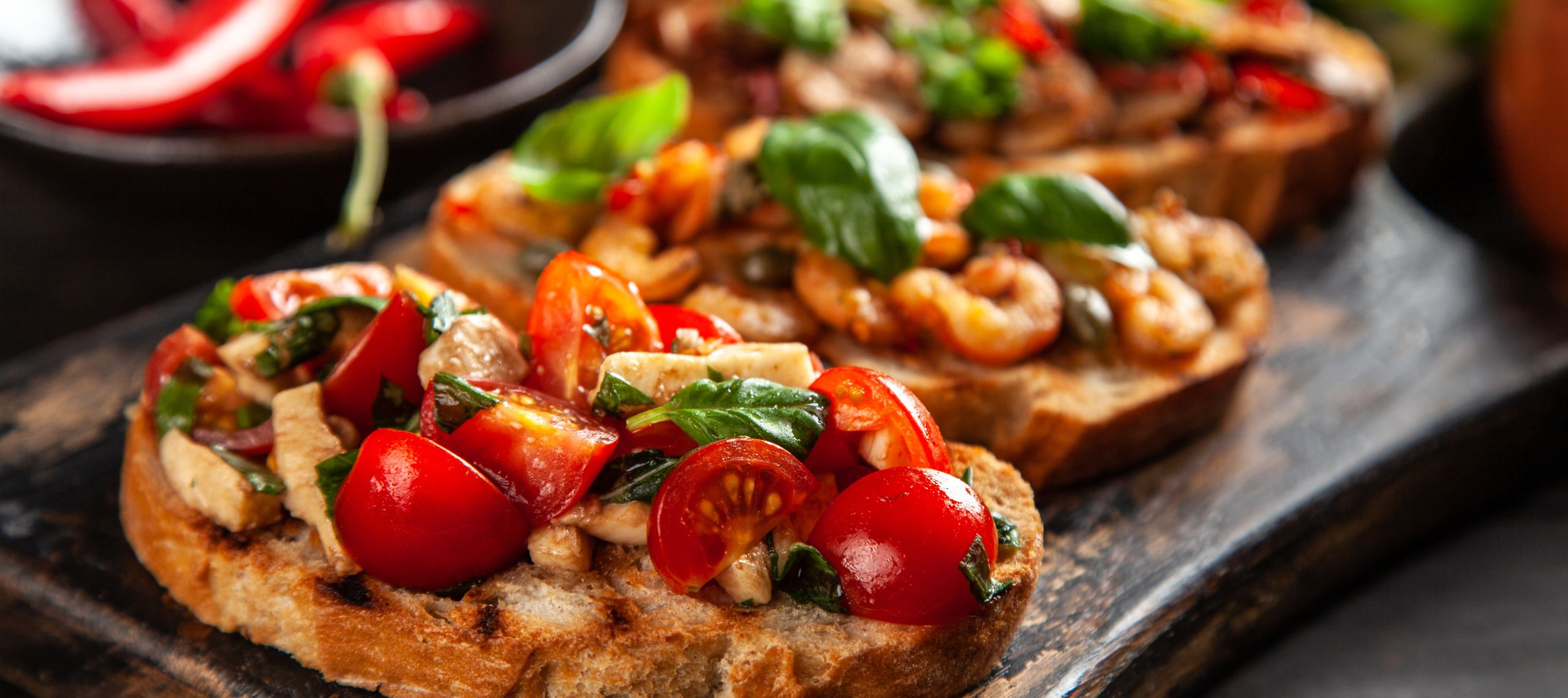 Bruschetta sind auf einem Teller sehr geschmackvoll angerichtet. Auf einem der Bruschetta sieht man Garnelen