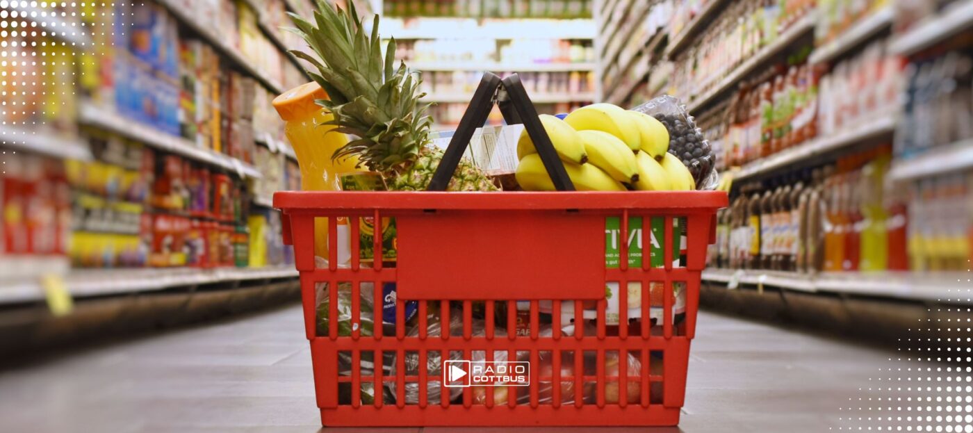 Einkaufskorb der rot ist und auf dem Boden steht. In einem Supermarktgang ist der gefüllt mit Lebensmitteln