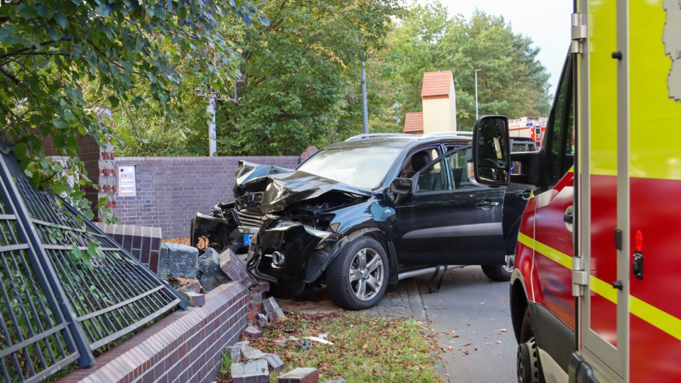 Ein schwarzer Toyota ist in einen Grundstückszaun gekracht, der Rettunswagen steht neben dem kaputten Fahrzeug