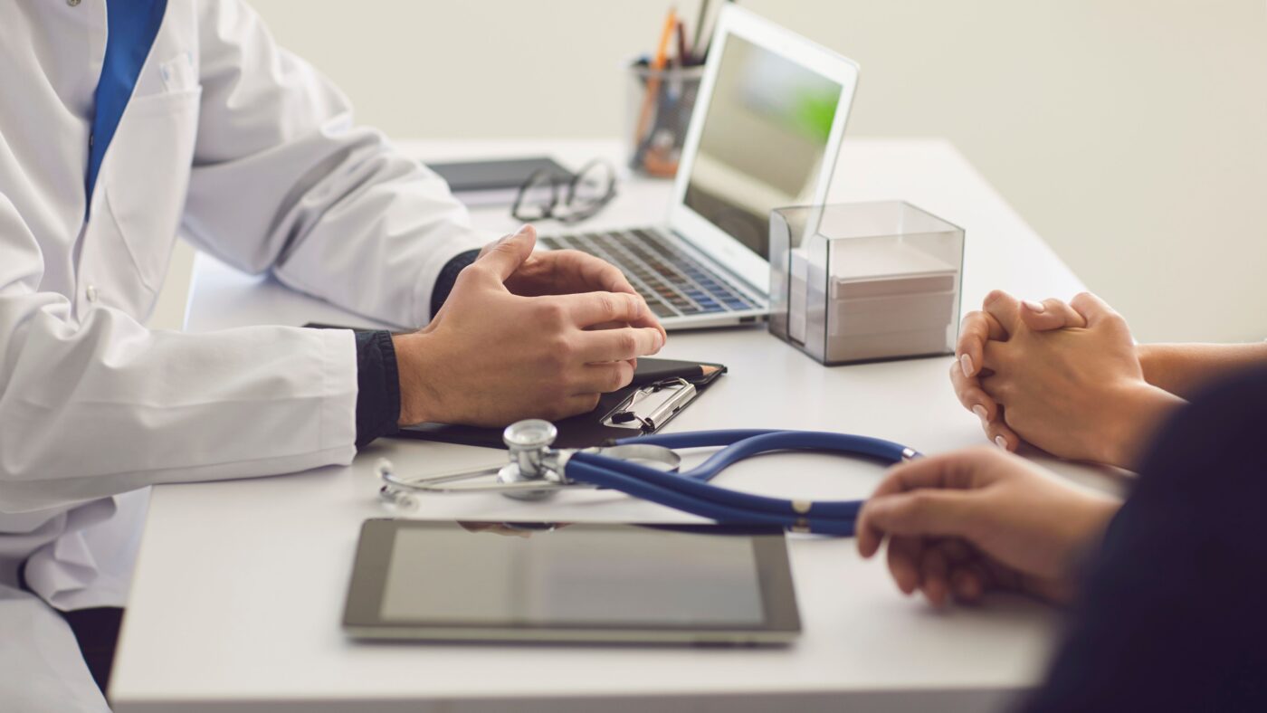 Ein Arzt im Kittel spricht mit Patienten, man sieht nur die Hände der Personen
