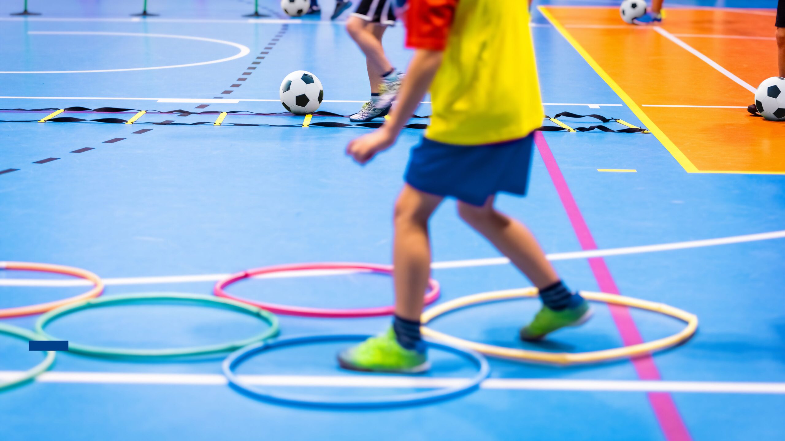 Kinder machen Sport in einer Halle und absolvieren einen Parcour mit Reifen auf dem Boden