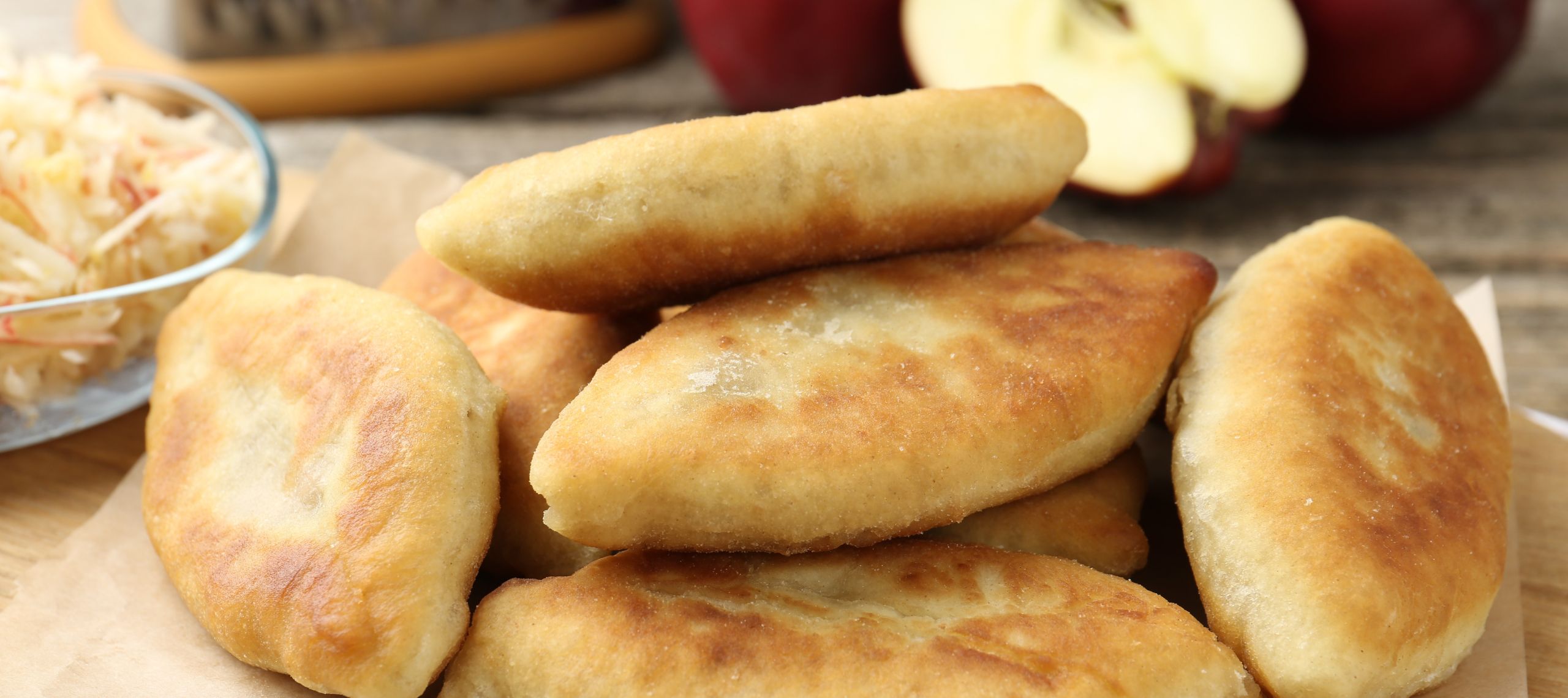 Fisch gebackene Piroschki nach einem Rezept aus Osteuropa liegen auf einem Tisch im Herbst, im Hintergund ist ein aufgeschnittener Apfel zu sehen