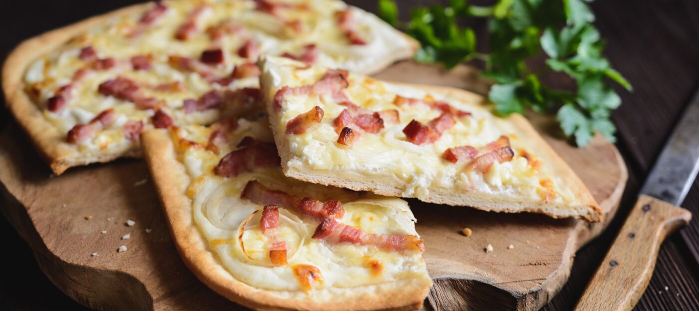 Zwiebel-Speck-Kuchen liegt angeschnitten auf einem Holzbrett