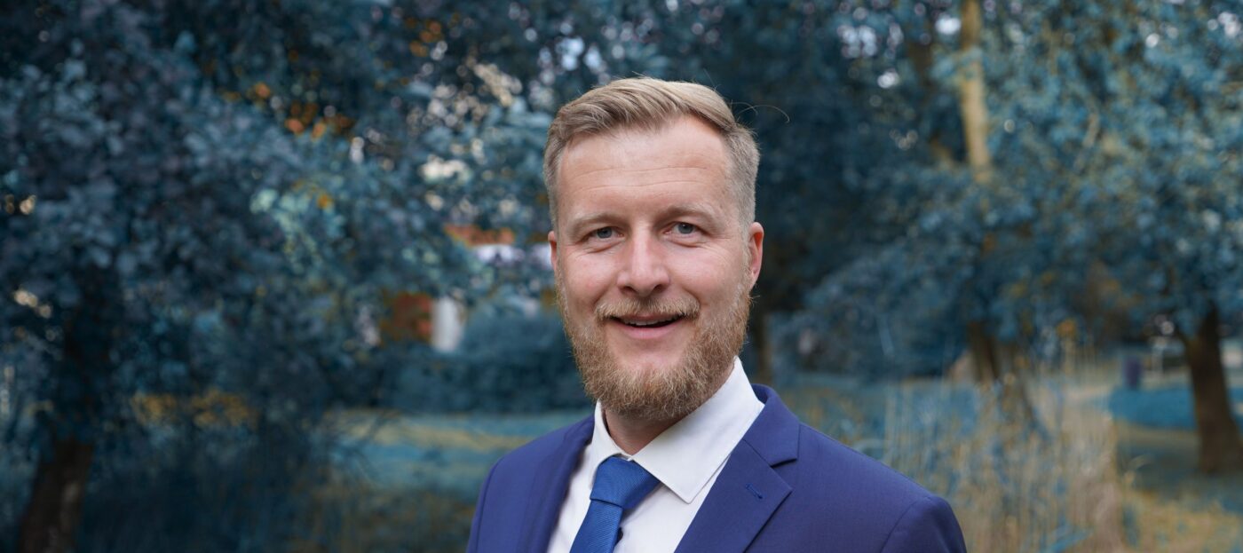 Der Kandidat für die Landratswahl 2026 im Spree-Neiße, Martin Heusler im Porträt vor einer grünen Waldlandschaft