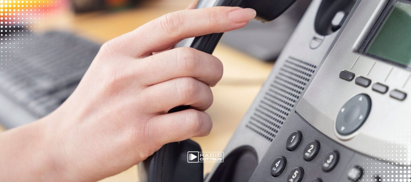Eine Frauenhand nimmt den Hörer eines Telefons ab