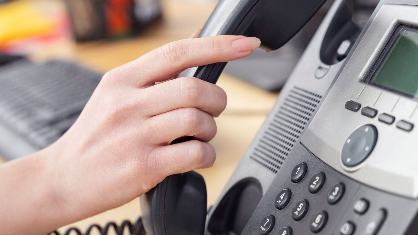 Eine Frauenhand nimmt den Hörer eines Telefons ab