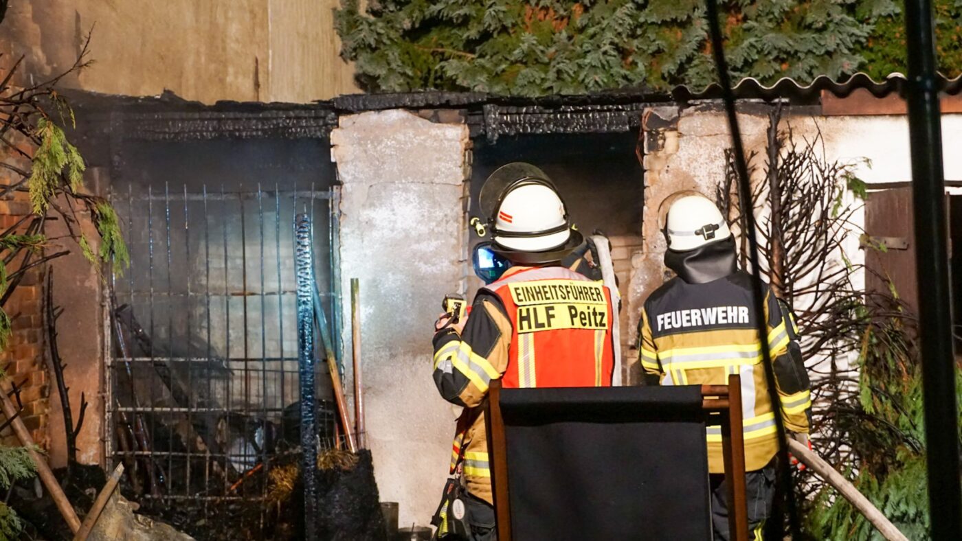 Zwei Feuerwehrmänner stehen vor einem Gebäude und löschen einen Brand