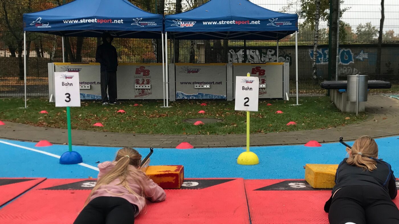 Zwei Schülerinnen liegen auf dem Bauch am Schießstand und versuchen die Biathlonziele zu treffen